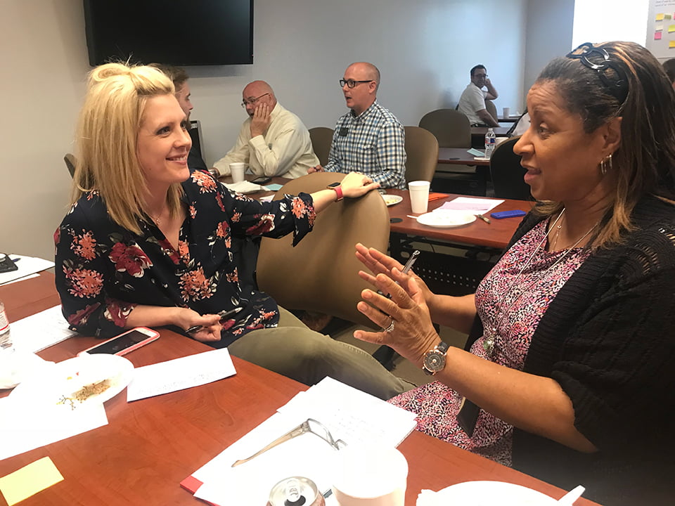 Two women discussing at a training with others in the background