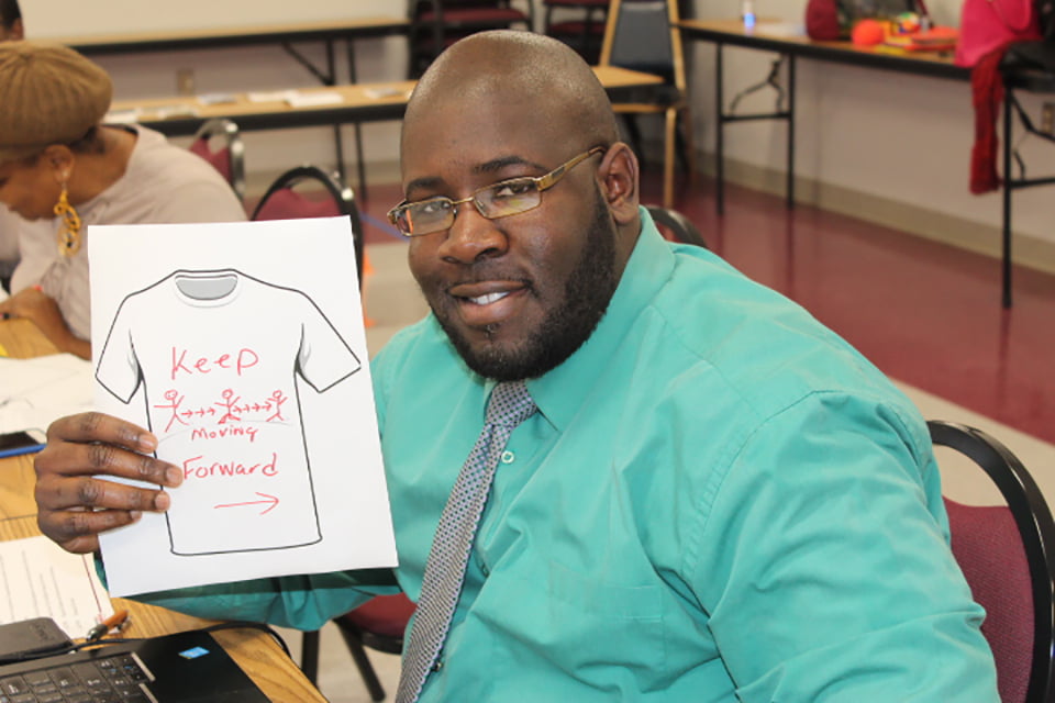Gentleman holding a picture of a shirt with 'Keep Moving Forward' written on it.'